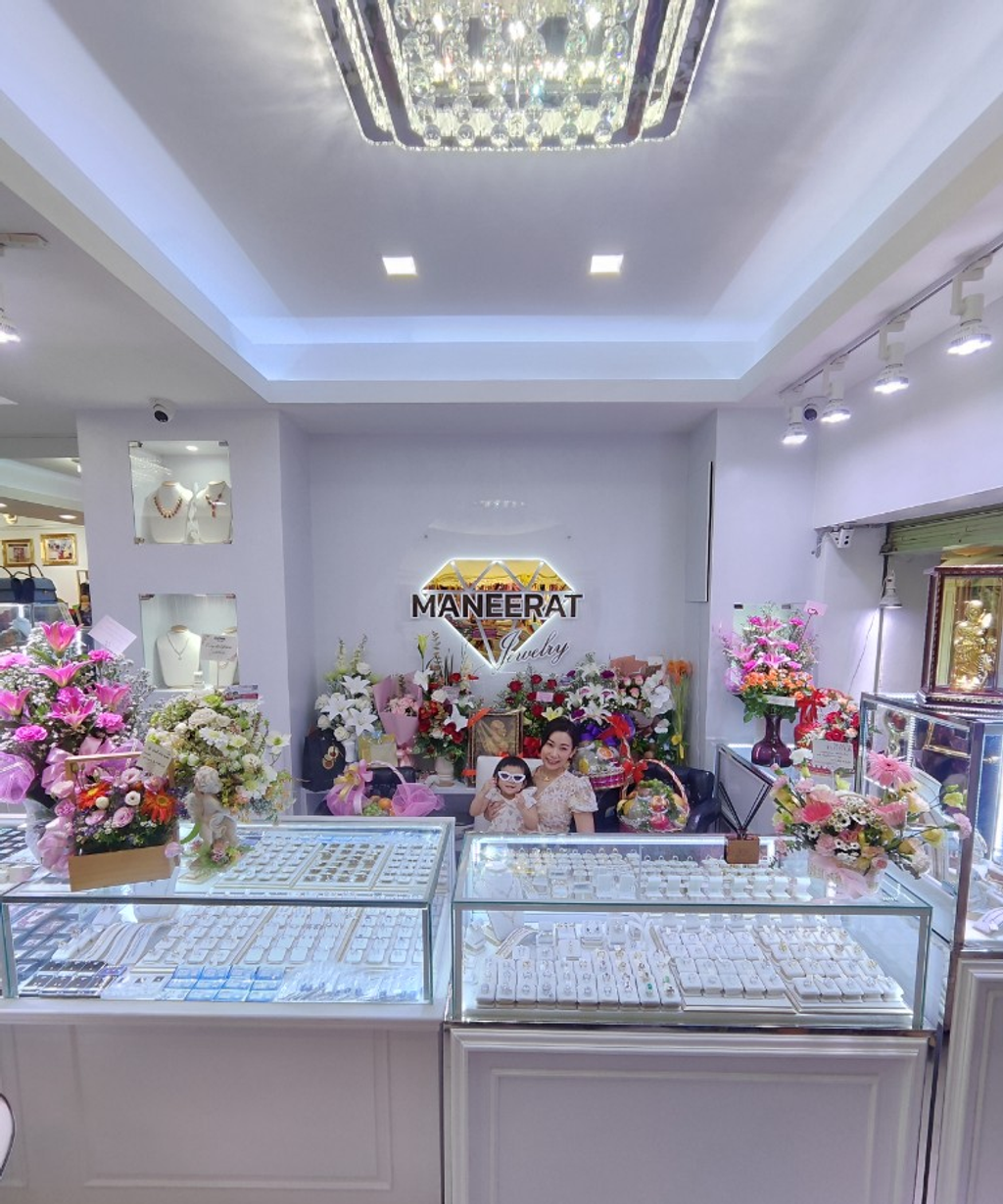 Maneerat Jewelry store interior with display cases, flowers, and illuminated logo